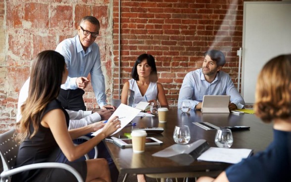 Équipe de partenaires divers homme d'affaires latin mature et femme d'affaires européenne discutant du projet sur une tablette assis à table au bureau