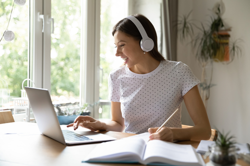 businesswoman with headphones on, typing on a laptop