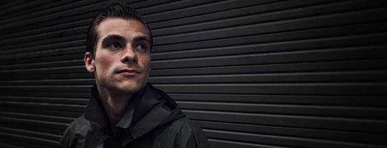 Picture of young man in black jacket standing in front of the black wall