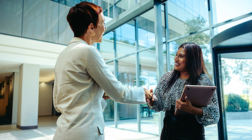 Professional businesswomen shaking hands in a bright modern office lobby